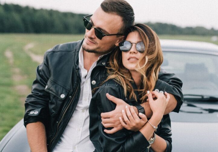 stylish-couple-in-sunglasses-embracing-near-luxury-car-in-4541585